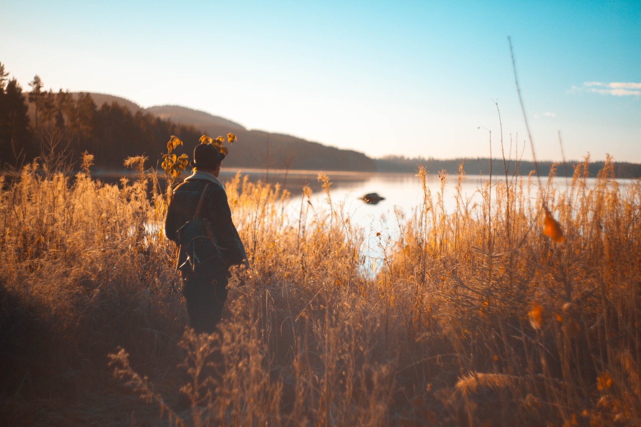 man standing in a field looking over a lake in the afternoon